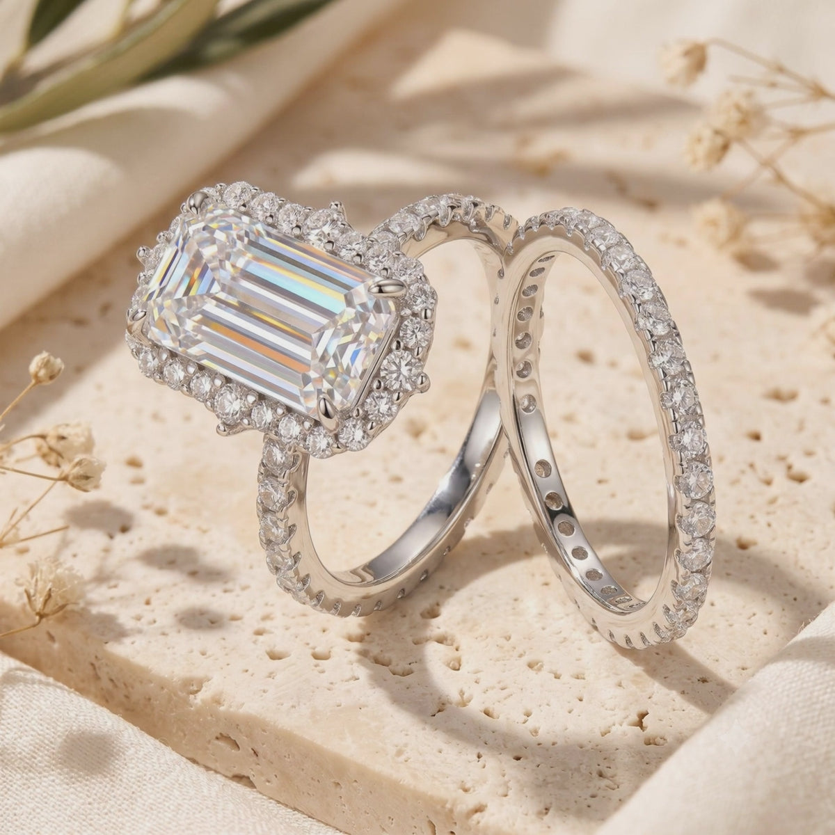 Silver-tone emerald-cut halo ring and matching pavé eternity band displayed on a textured stone surface.