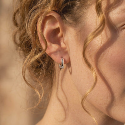 Silver huggie hoop earring with a round moissanite shown worn on a model’s earlobe in close-up side view.