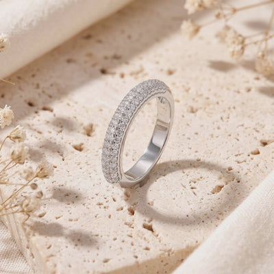 Silver triple-row pavé band standing upright on a porous beige stone surface, showing its polished inner band.