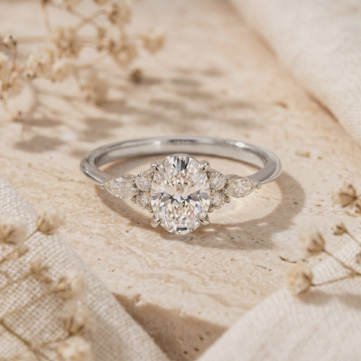 Silver oval moissanite ring with cluster side stones resting on a beige stone surface.