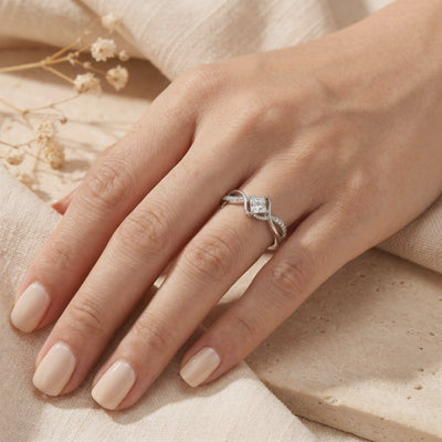 The silver princess-cut moissanite ring with a twisted band worn on a hand against a neutral background.