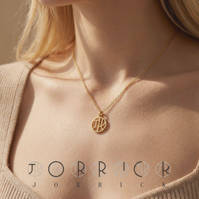 Gold-toned circular monogram necklace worn on a model in a ribbed beige top, showing the chain and cut-out pendant
