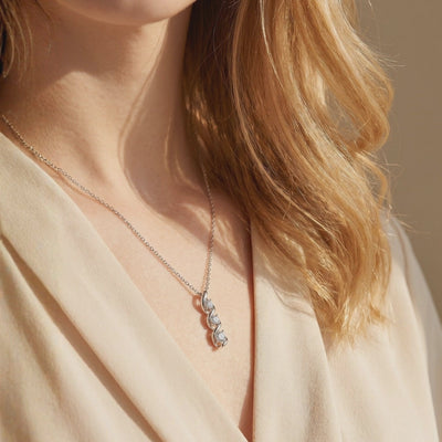 Silver helical pendant necklace with three cascading round moissanite stones, shown worn on a model.