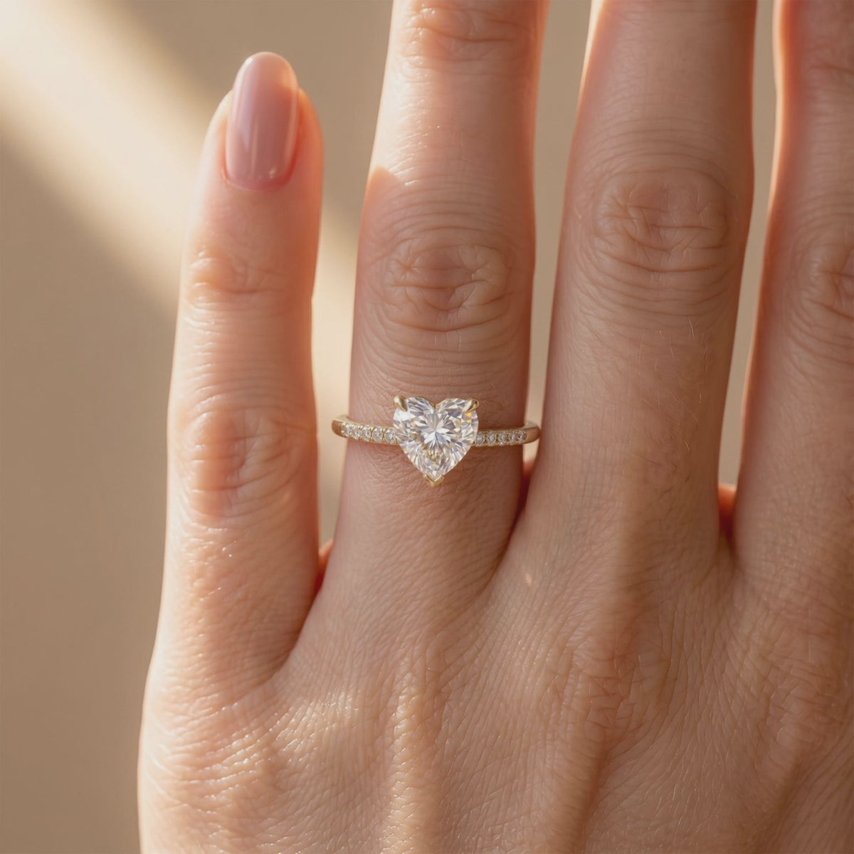 Close-up of a heart-cut moissanite solitaire ring with a pavé band worn on a finger.