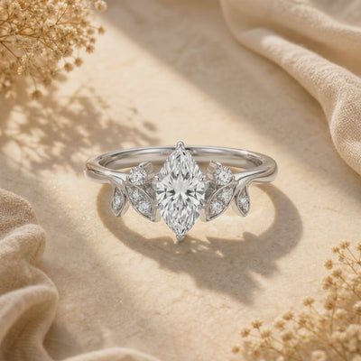 Front-facing close-up of a silver marquise-cut moissanite ring with leaf-shaped side accents on fabric