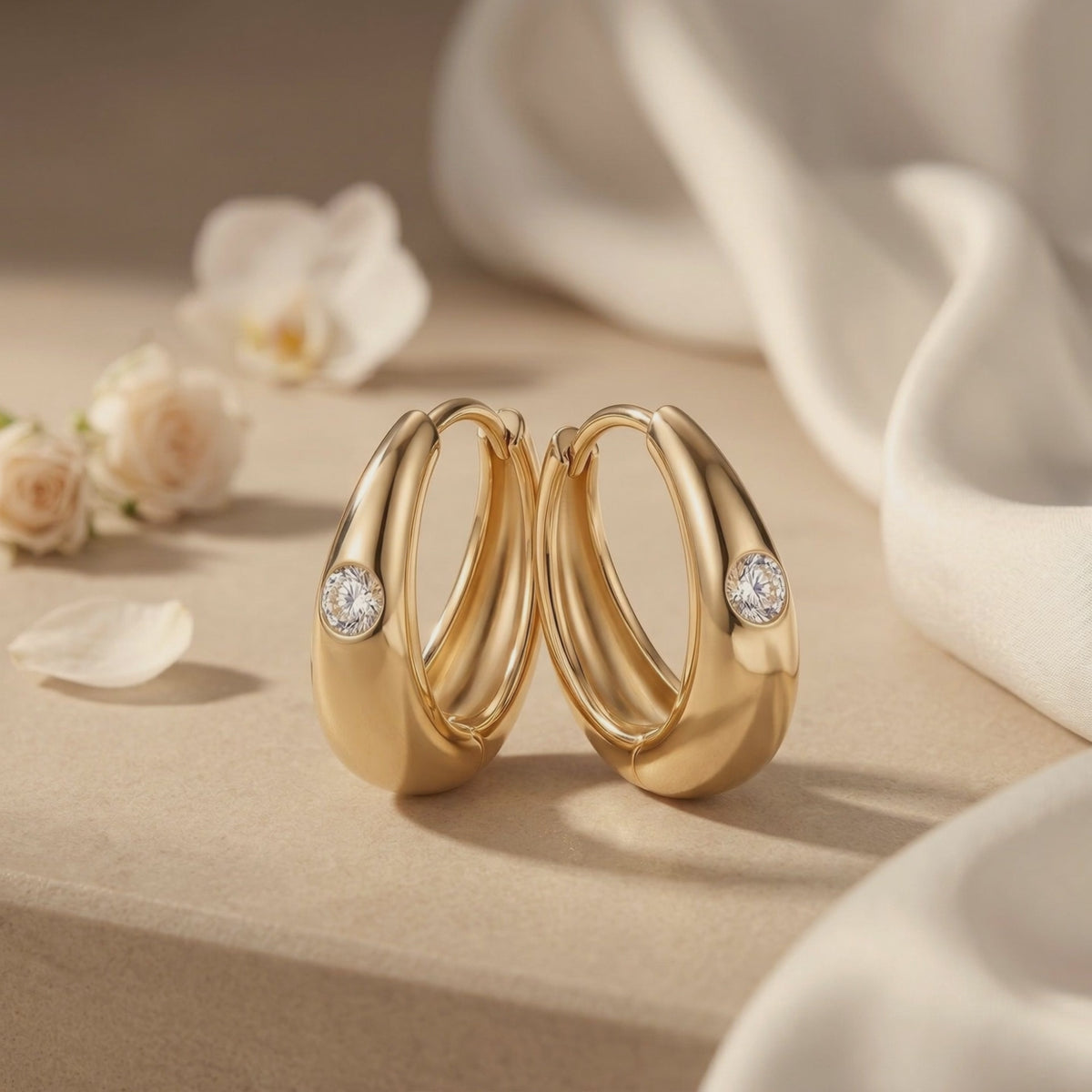 Pair of gold-tone tapered huggie hoop earrings with round moissanite stones, standing on a neutral surface.