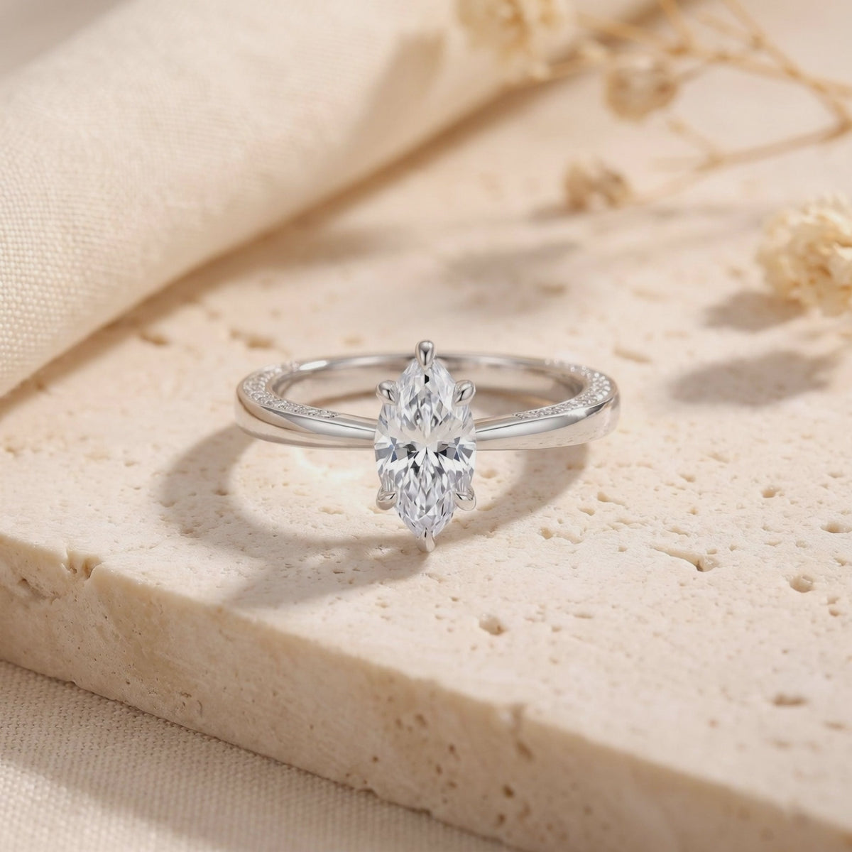 Close-up of a silver ring with a marquise-cut clear center gem displayed upright on a beige stone surface.