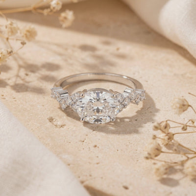Silver ring with a horizontal oval center stone and clustered side accents, displayed on a beige stone slab.