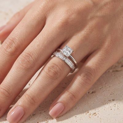 Silver ring set worn on a finger, featuring a square clear center stone and a baguette-set band.