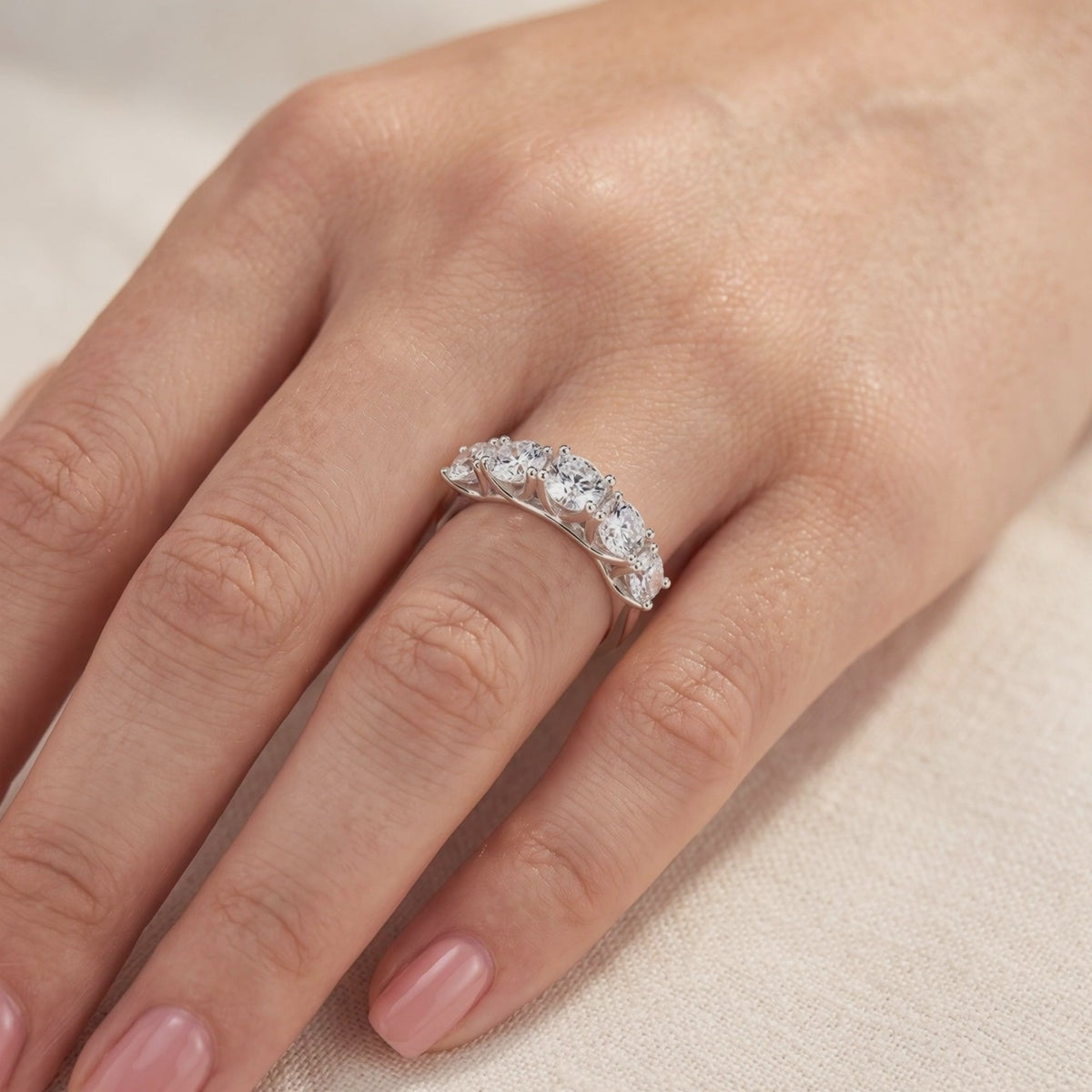 Five-stone silver ring with graduated clear round stones shown on a hand