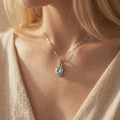 Model wearing a silver necklace with an oval light-blue simulated aquamarine pendant and halo