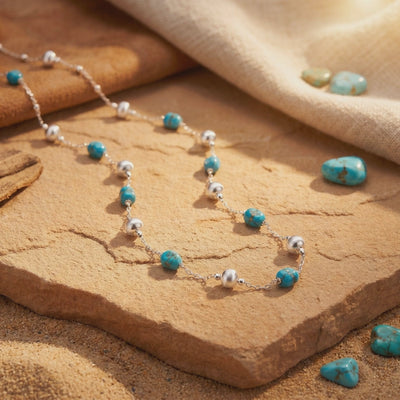 Pueblo turquoise necklace with silver and turquoise beads laid across a tan stone slab in sunlight.