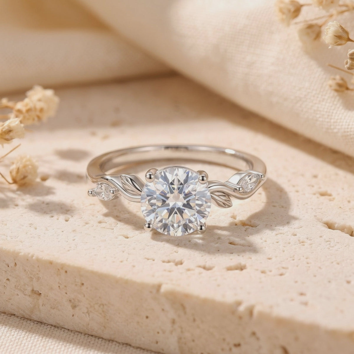 Close-up of a silver leaf-motif ring with a round clear center stone resting on a beige stone slab.