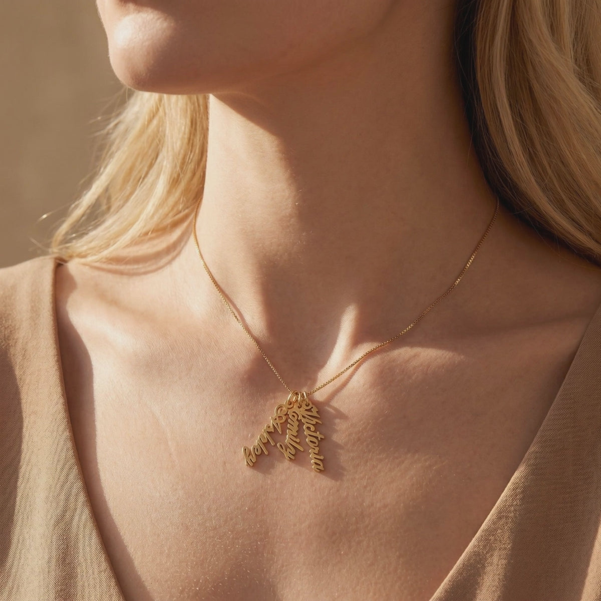 Gold-tone custom name necklace with three script pendants shown worn on a woman's neck.