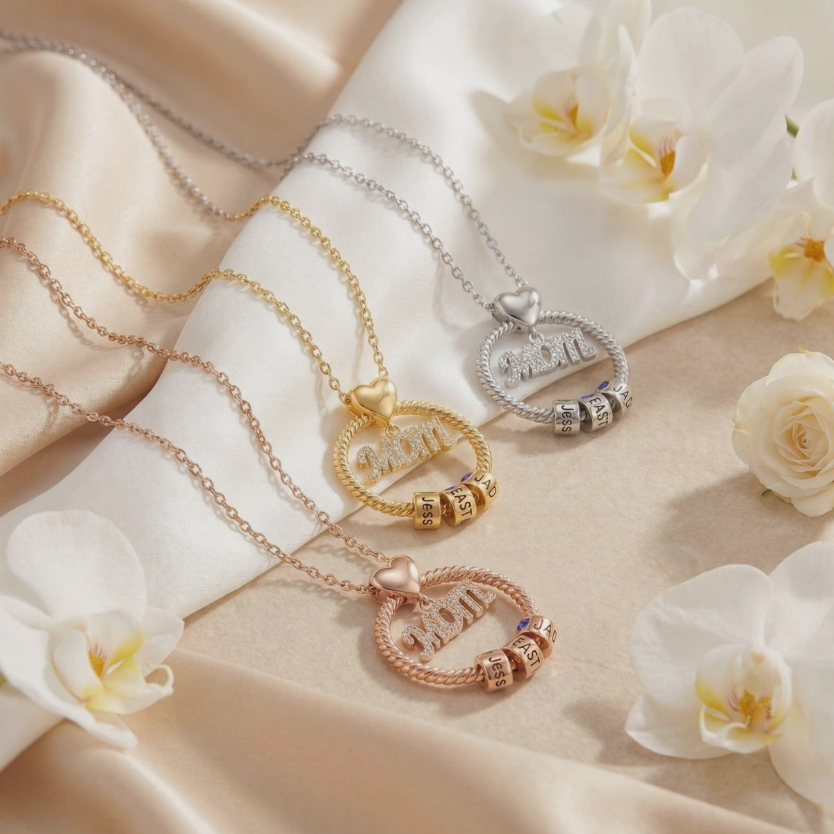 Gold-, silver-, and rose gold-tone MOM necklaces displayed on silk fabric among white flowers.