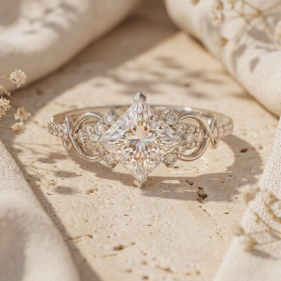 Macro view of a silver-toned ring with a kite-set square center stone and detailed filigree shoulders.
