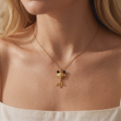Gold-tone goldfish pendant necklace with black eyes worn around a woman's neck.