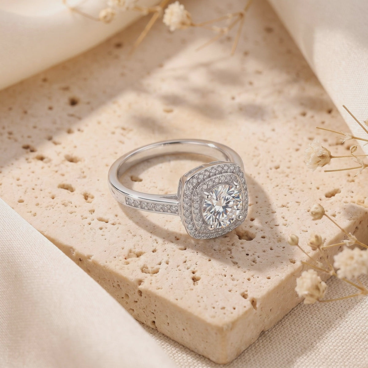 The Juliette Ring on a beige porous stone surface, showing a round center stone, square double halo, and pavé band.
