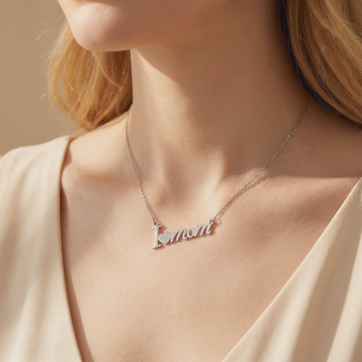 Model wearing a silver-finish script necklace reading “I [heart] mom” at the collarbone.