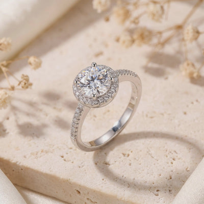 Silver round halo ring with an accent-paved band resting upright on a textured stone surface.