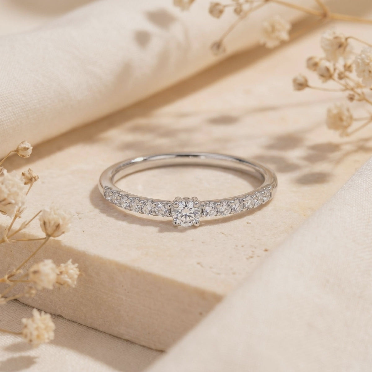 Silver pavé ring with a round center moissanite stone resting on a stone slab.
