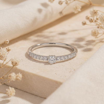 Silver pavé ring with a round center moissanite stone resting on a stone slab.