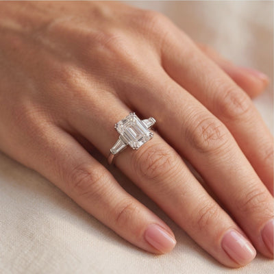 Video preview of a silver three-stone ring with an emerald-cut center, worn on a hand.