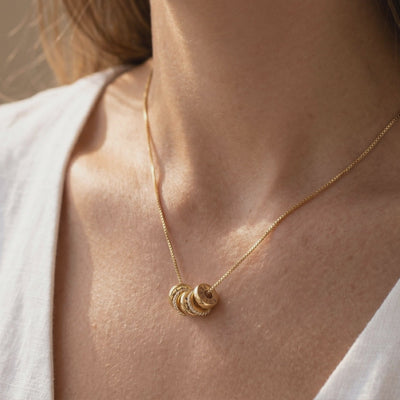 Gold-tone chain necklace with engraved name charms and sparkling stone-set rings, worn on a woman's neck.