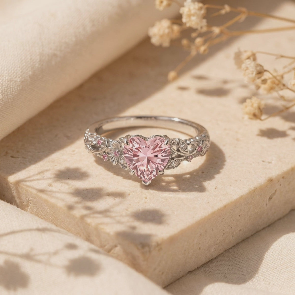 Close-up view of The Rosalique Ring, a solid gold ring with a heart-shaped pink simulated diamond centerpiece and floral filigree band, resting on a stone surface.