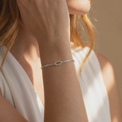 Silver double snake-chain knot bracelet worn on a woman's wrist.
