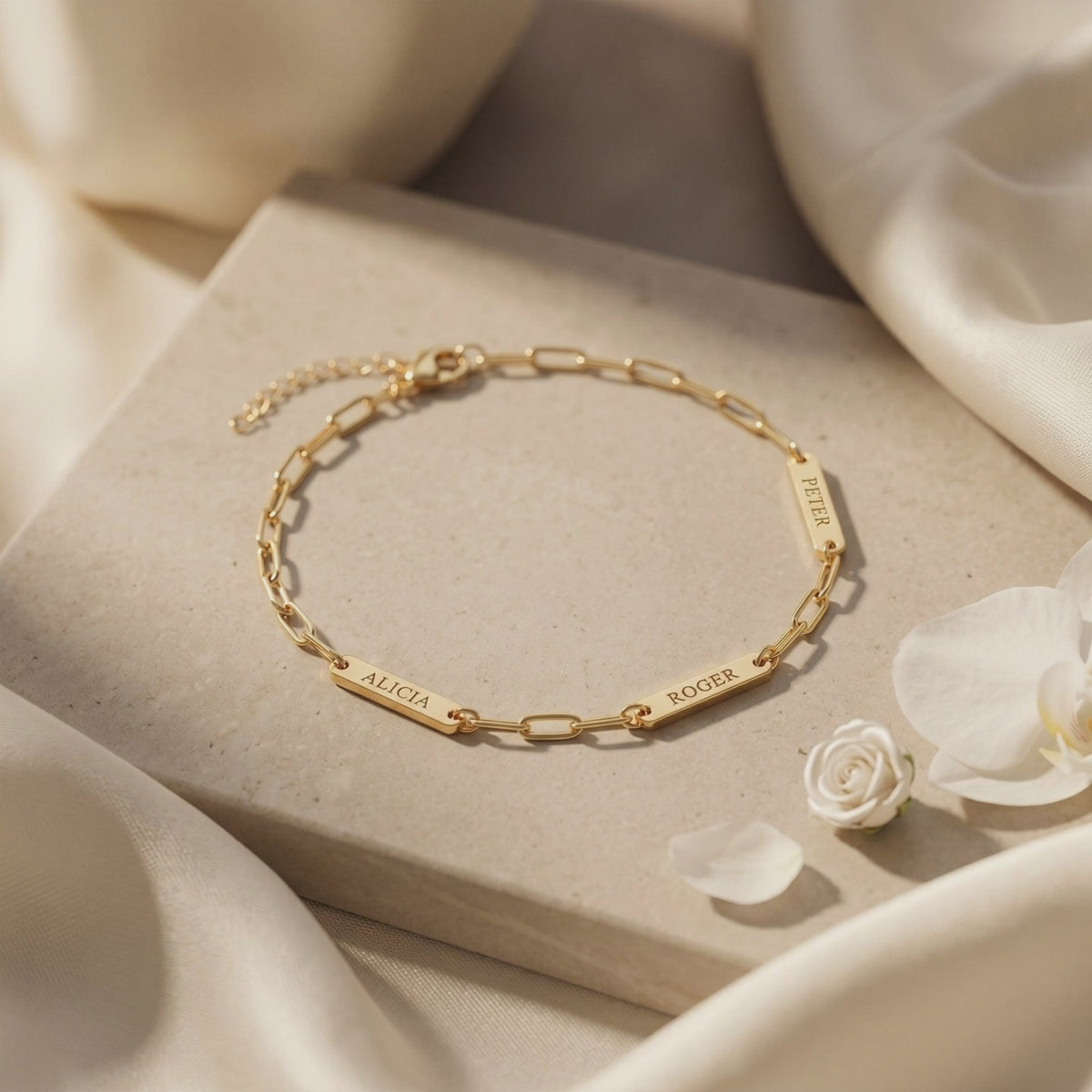 Gold-toned chain bracelet with three engraved name plates displayed flat on a stone slab.