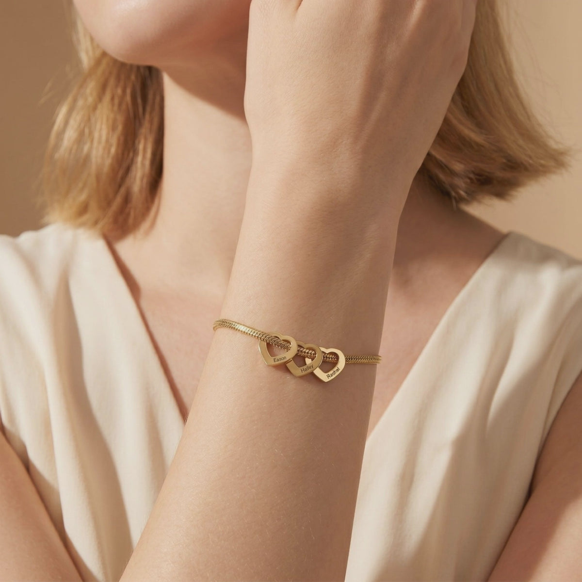 Gold-tone snake chain bracelet featuring three engraved heart charms, worn on a model's wrist.