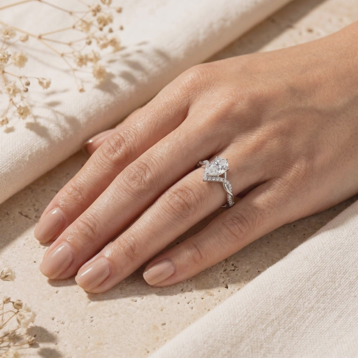 Hand wearing a silver pear-cut moissanite ring with a twisted pavé band and chevron accent.
