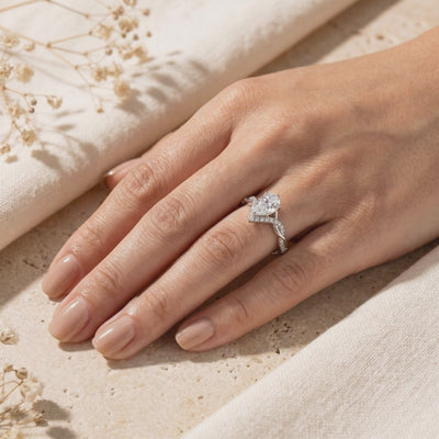Hand wearing a silver pear-cut moissanite ring with a twisted pavé band and chevron accent.