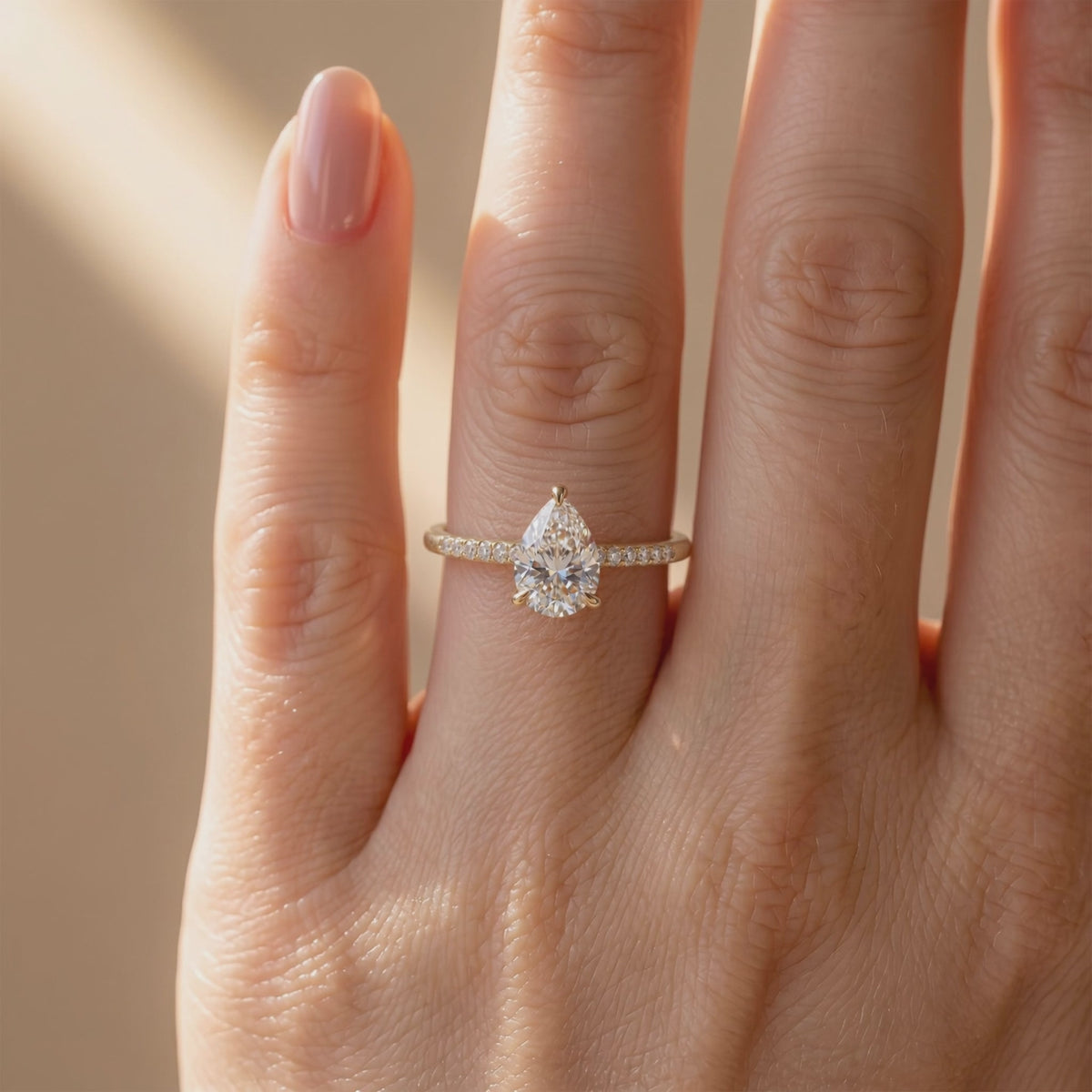 Pear-cut solitaire ring with a pavé band worn on a finger in a close frontal view.