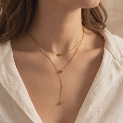 On-model view of a gold-toned double-layered lariat necklace with polished sphere accents.