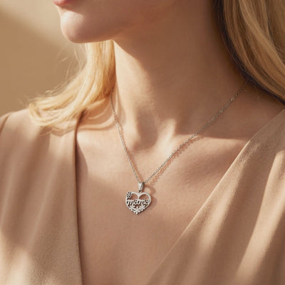 Silver heart necklace with mama script and floral cutouts worn around a model's neck over a beige top.