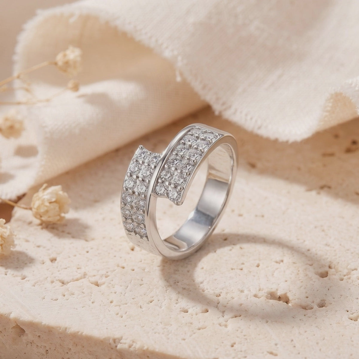 Silver bypass ring with pavé clear stones displayed upright on a textured stone surface.