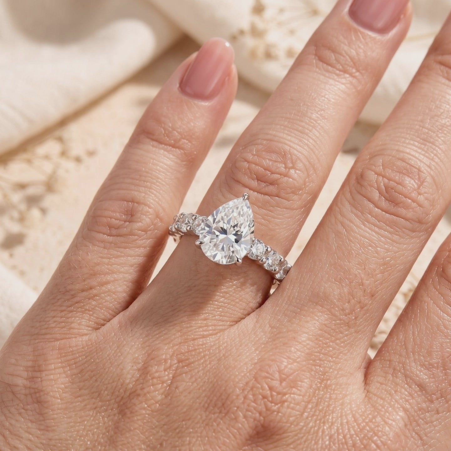 Silver ring with a pear-cut center stone and stone-set band worn on a hand.