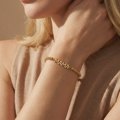 Gold-tone beaded bracelet with block letters spelling MAMA, worn on a wrist.