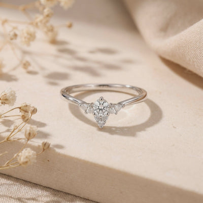 Silver-toned ring with a round clear center stone and smaller cluster accents, displayed on a light surface.