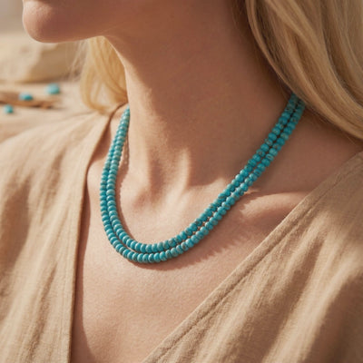 Double-strand turquoise bead necklace worn around a model’s neck over a beige top, resting near the collarbone.