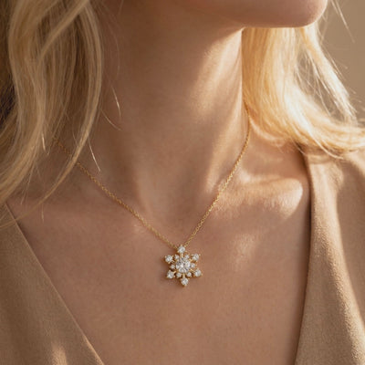 Gold-tone snowflake pendant necklace with clear sparkling stones, worn on a woman's neck.