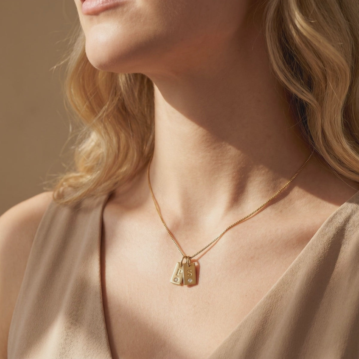 Video preview of a model wearing a gold-tone necklace with two engraved P and S tag pendants.