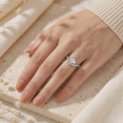 Silver bypass ring with a bezel-set pear-cut moissanite, shown worn on a person's hand.