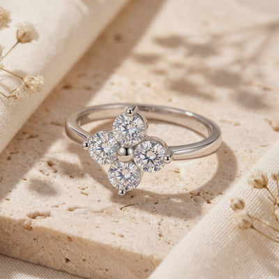 Close-up of the silver clover ring resting on a textured stone tile, showcasing four round cubic zirconia.
