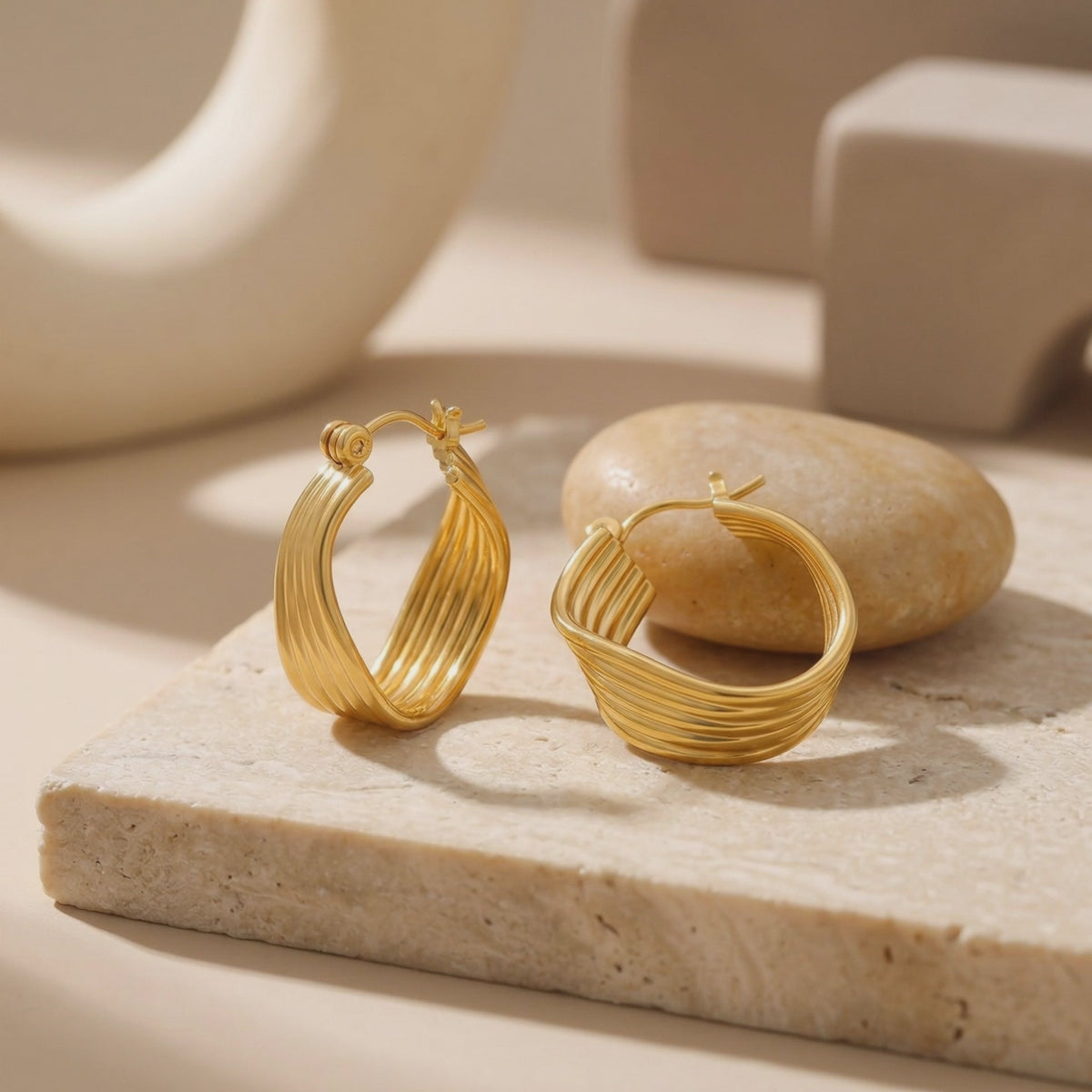 Pair of gold-toned ribbed multi-strand hoop earrings resting on a beige stone block.