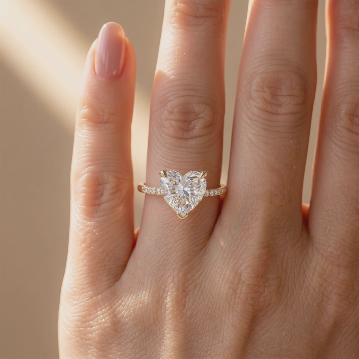Top view of a gold-tone ring with a large heart-cut clear center stone and pavé band worn on a finger