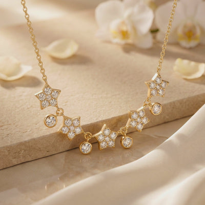 Gold-tone star necklace draped over a beige ledge, with five jeweled stars and four dangling round bezels.