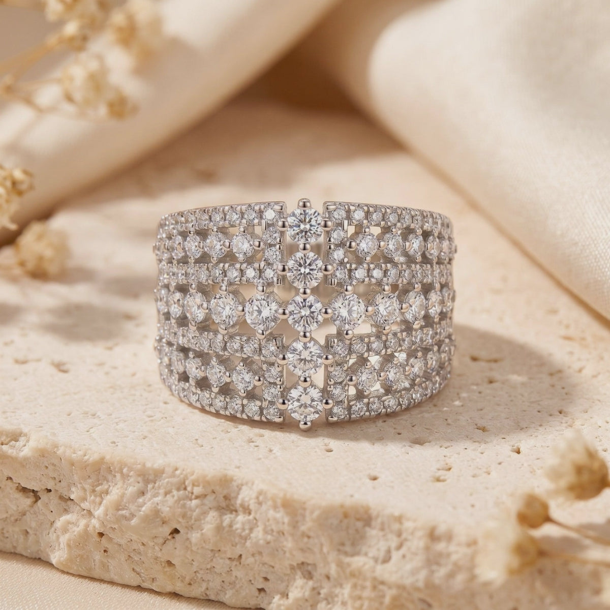 Front view of the wide silver Eleonora ring with a multi-row clear stone grid, resting on a textured stone surface.